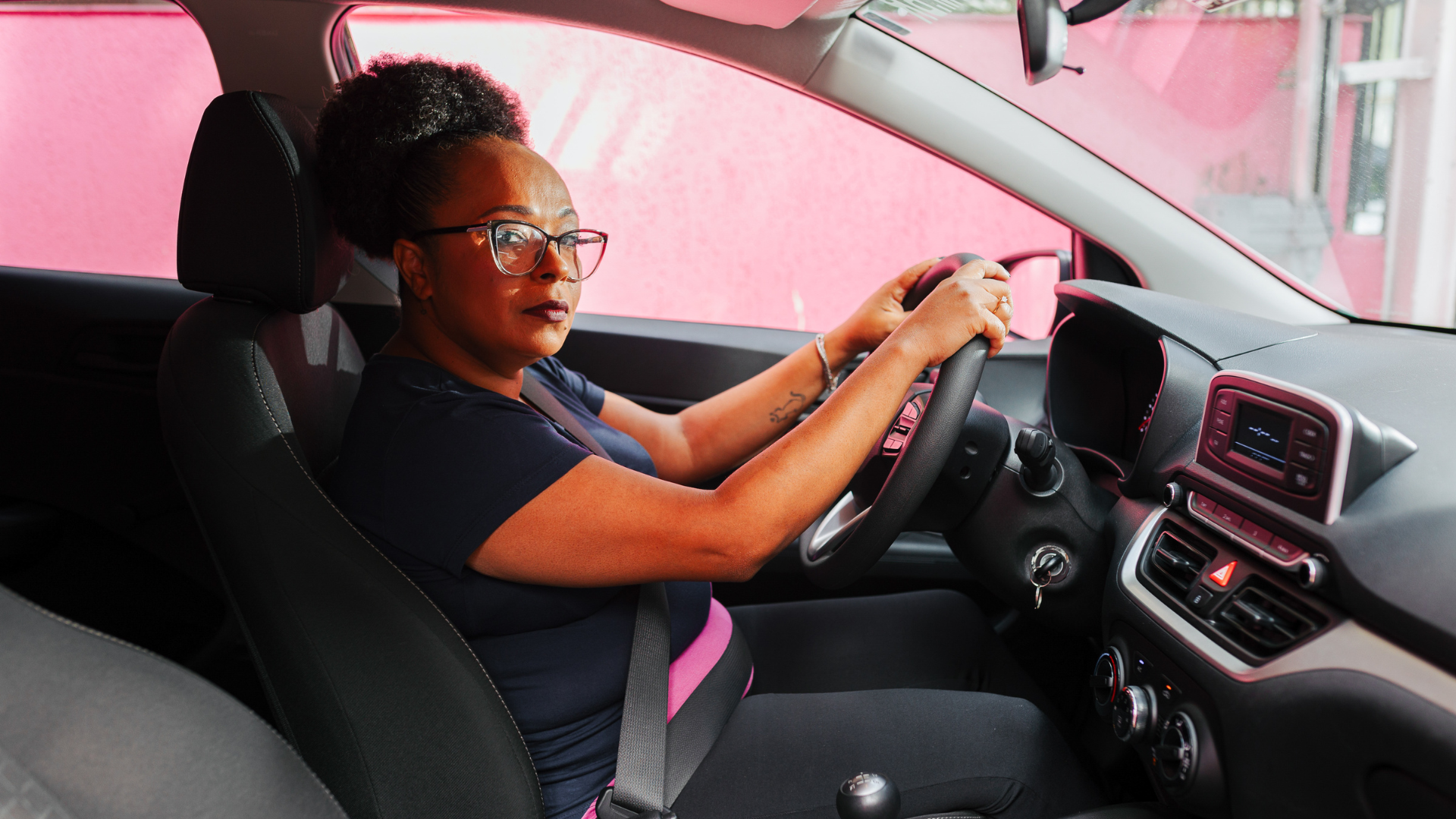 Mulher sentada no carro com as mãos no volante aprendendo a dirigir